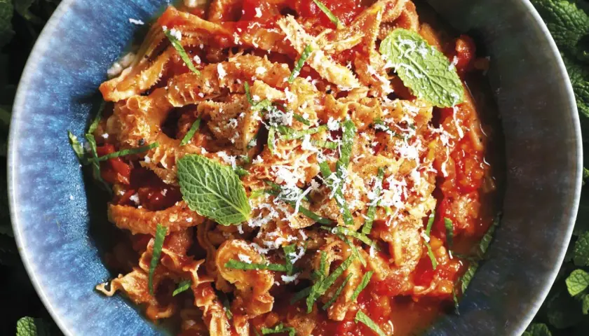 Un piatto fumante di trippa alla romana, condita con pomodoro, pecorino e menta fresca, servita in una ciotola blu.