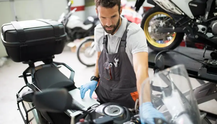 Mecánico revisa en laptop por qué la moto se para en marcha y no arranca.