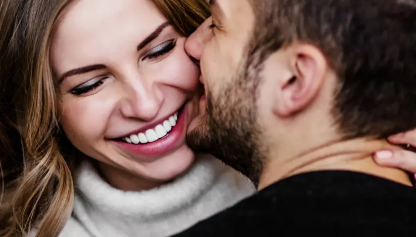 Uśmiechnięta kobieta, której mężczyzna szepcze coś do ucha. Czy to koniec nudy w związku?