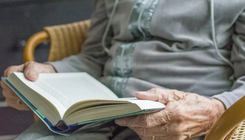 Dłonie seniora trzymają otwartą książkę. Czytanie to świetne pomysły na zajęcia z seniorami, rozwijające wyobraźnię i wiedzę.