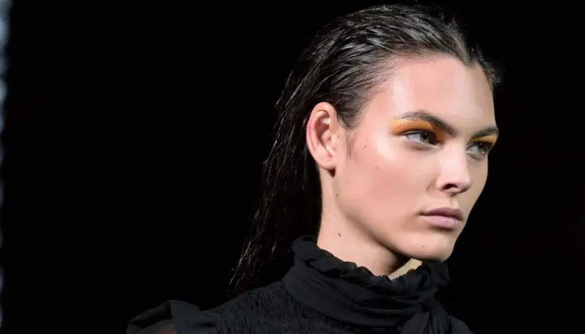 Modelka z błyszczącymi, mokrymi włosami i złotymi cieniami do powiek. Efekt wet look podkreśla jej urodę.