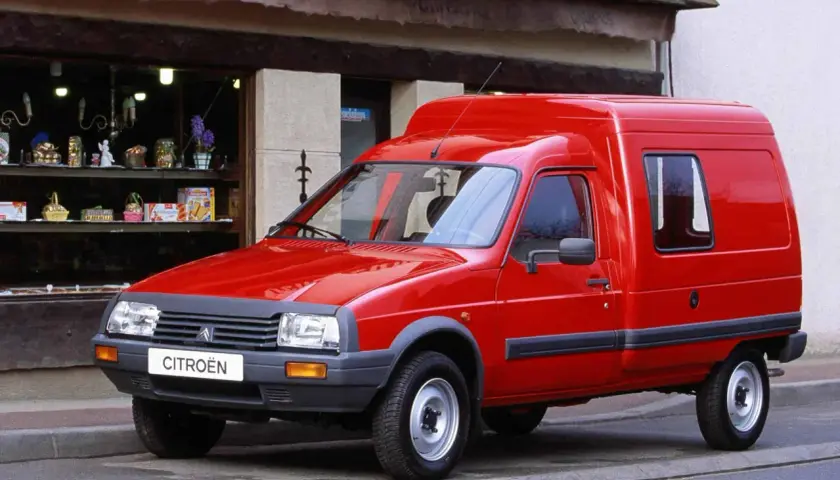 Czerwony van Citroen C15 zaparkowany przed sklepem z witryną pełną drobnych przedmiotów.