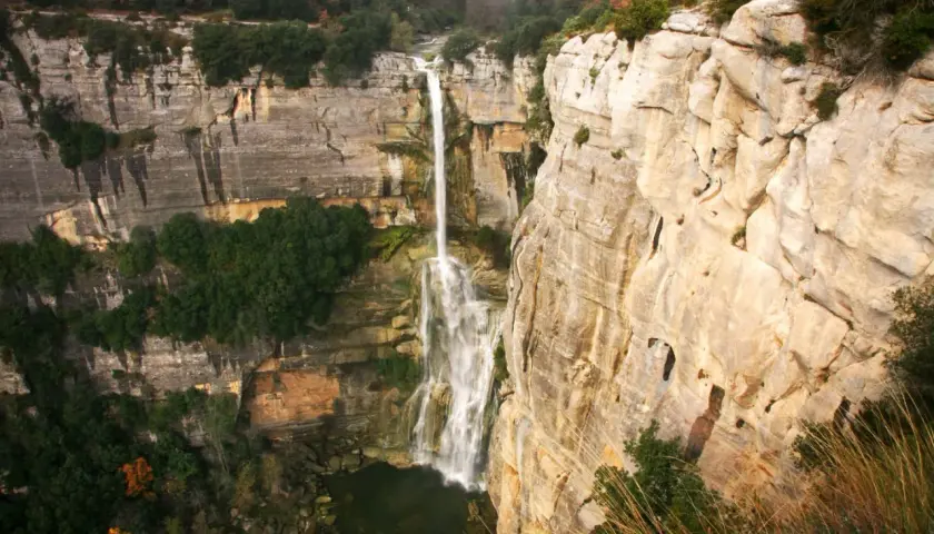 El imponente salt de Sallent cae desde lo alto de acantilados rocosos, rodeado de vegetación exuberante y un paisaje natural impresionante.