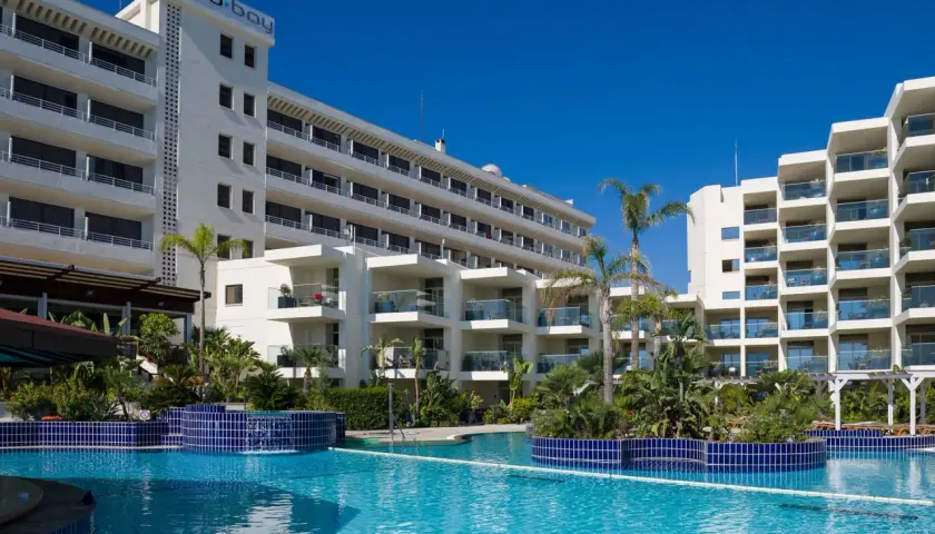 Basen hotelowy Capo Bay w Protaras z palmami i białymi budynkami hotelowymi pod błękitnym niebem.