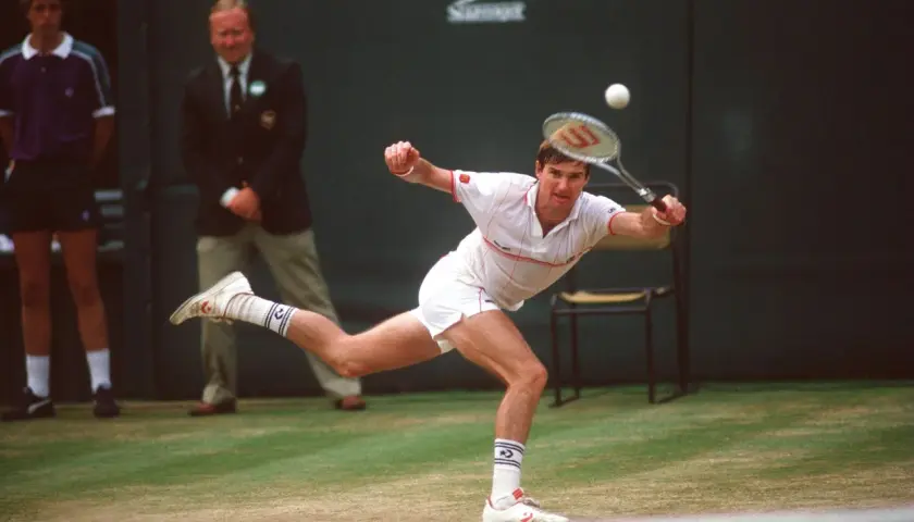 Jimmy Connors w akcji, uderza piłkę na trawiastym korcie. W tle sędzia i chłopiec podający piłki.