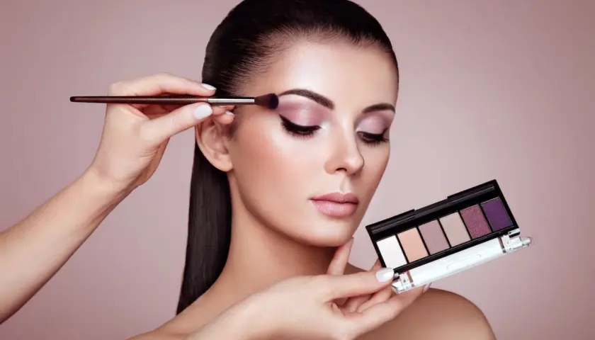 Kobieta zmysłowo maluje powieki, tworząc efekt latte makeup. W dłoni trzyma paletę cieni do powiek.