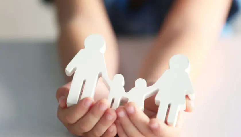 Hände halten weiße Holzfiguren einer Familie. Dies symbolisiert die Verantwortung für ein Kind und die finanzielle Unterstützung, die damit einhergeht.