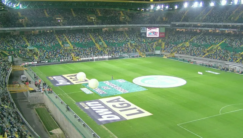 Widok na pełny stadion Sporting Lizbona, z zieloną murawą, trybunami wypełnionymi kibicami i reklamami na boisku.