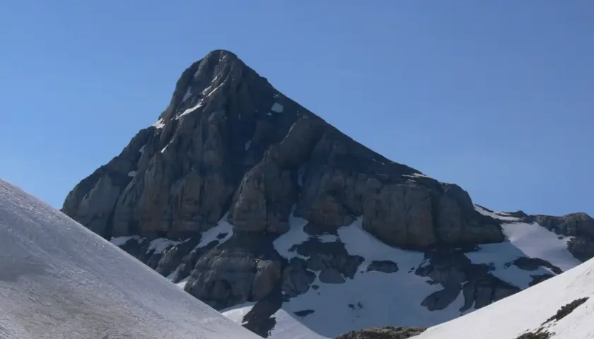 Majestuosa cumbre rocosa en el **valle de Belagua**, con nieve en sus laderas y un cielo azul intenso.
