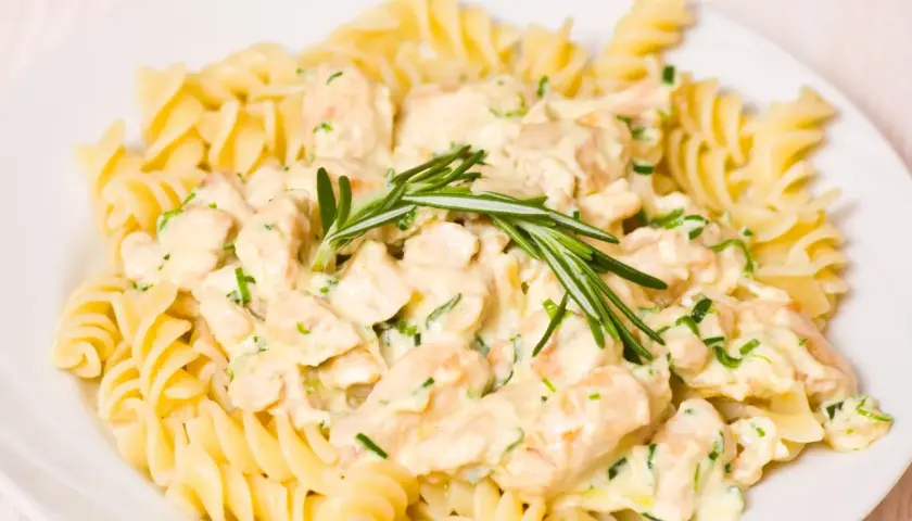 Pyszne tagliatelle z kurczakiem w kremowym sosie, udekorowane gałązką rozmarynu.
