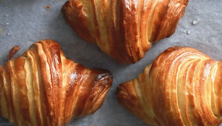 Croissant dorati e sfogliati, perfetti per una ricetta croissant fatta in casa. Si intravedono gocce d'acqua sulla carta da forno.