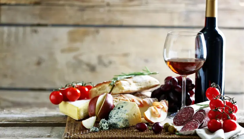 Degustacja najpopularniejszych win włoskich: kieliszek wina, butelka, sery, wędliny, pieczywo, winogrona i pomidorki.