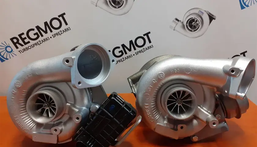 Dwa turbosprężarki, jedna z nich to hybrydowy turbo, na tle logo REG MOT.