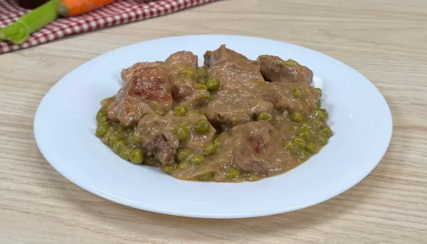 Un saporito spezzatino con piselli, servito su un piatto bianco, pronto per essere gustato.