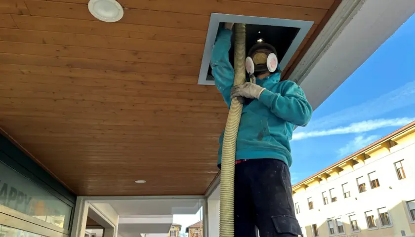 Operaio con maschera e guanti inserisce tubo in un'apertura del controsoffitto isolante termico in legno.