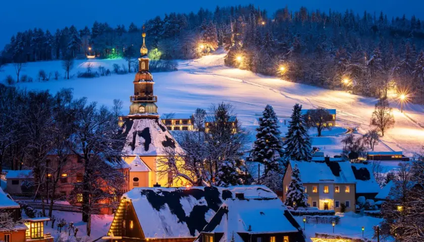 Ein verschneites Dorf in Deutschland, beleuchtet von warmem Licht. Perfekt für einen romantischen Winterurlaub.
