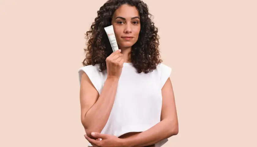 Mujer con cabello rizado sostiene un tubo de Cicalfate, crema reparadora para la piel.