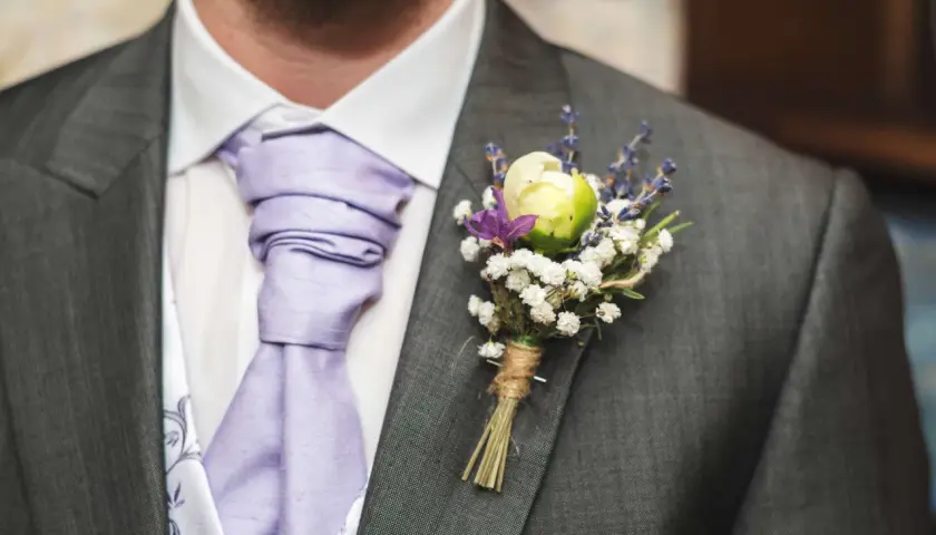 Elegancka butonierka co to? To ozdoba z kwiatów i lawendy przypięta do marynarki.