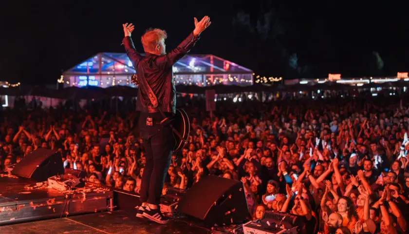 Artysta z podniesionymi rękami na scenie podczas koncertu. Tłum wiwatuje, tworząc niezapomniany line up Męskiego Grania.