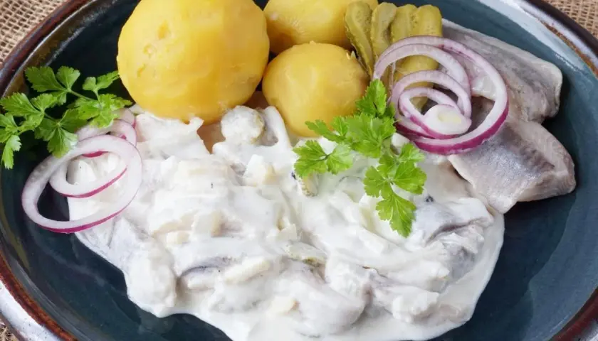 Marinierter Hering in cremiger Sauce mit Salzkartoffeln, Gurken und Zwiebelringen garniert.