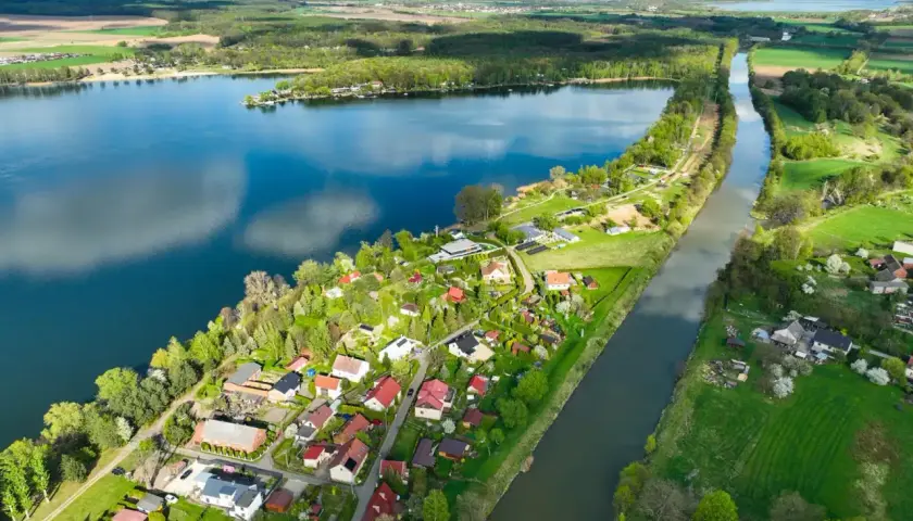 Malownicze pławniowice jezioro otoczone zielenią i domkami letniskowymi, z kanałem wodnym biegnącym równolegle.