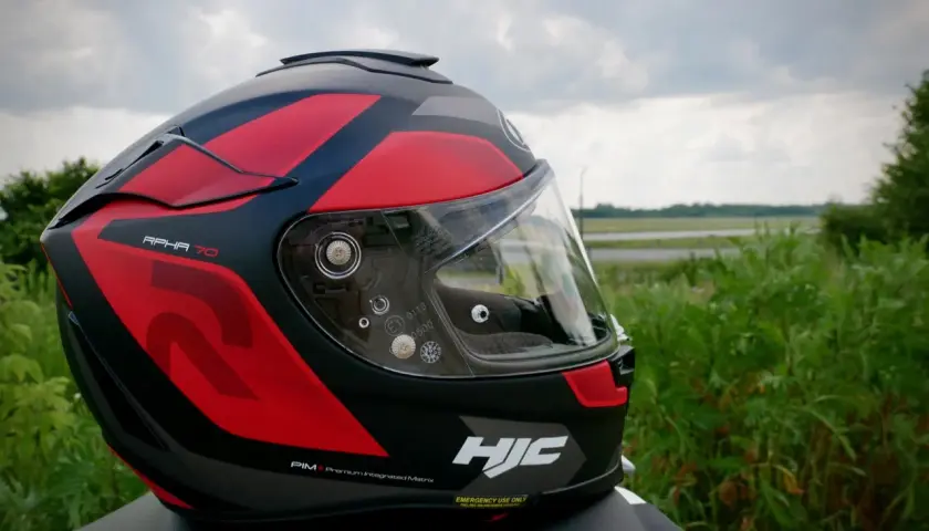 Kask motocyklowy HJC RPHA 70 w czerwono-czarne wzory, gotowy na przygodę na tle zieleni i nieba.