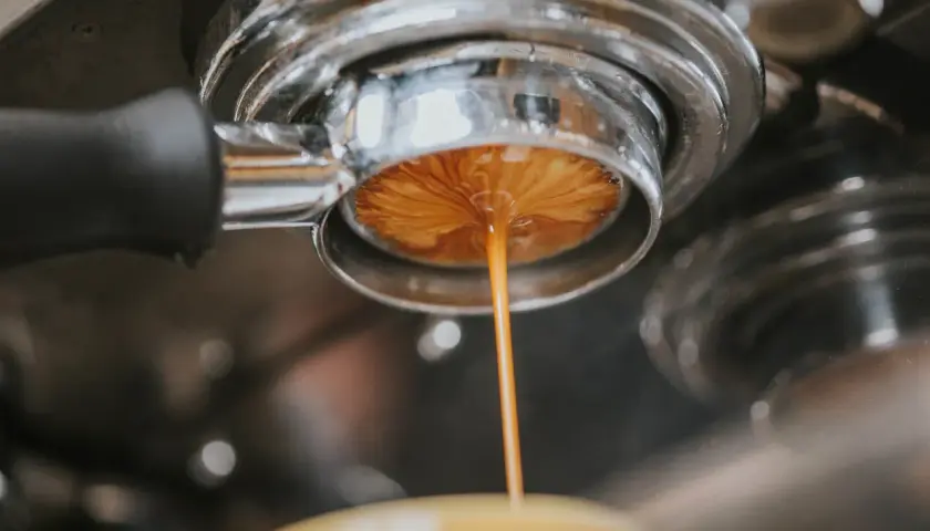 Espresso spływa do filiżanki, przygotowując americano. Dowiedz się, ile kofeiny ma americano.