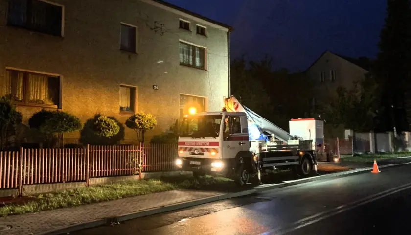 Samochód Tauron z podnośnikiem przy budynku, nocą. Zgłoszenie awarii w toku.