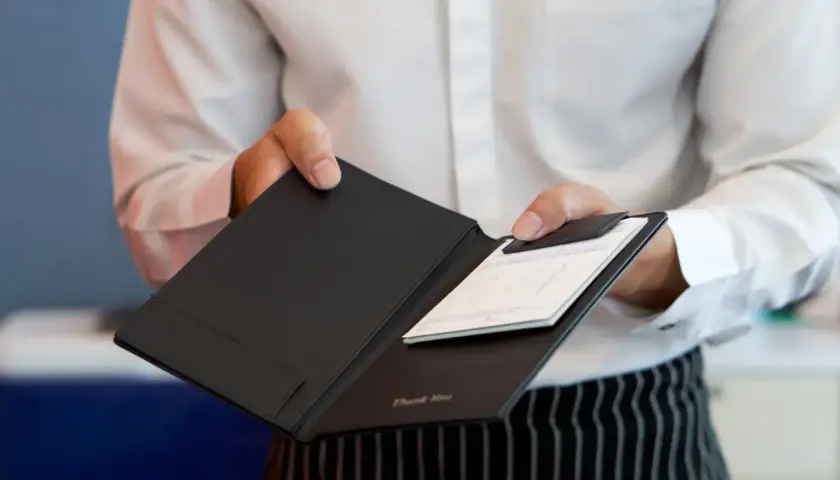 Kelner podaje rachunek do zapłaty, ułatwiając dzielenie rachunku w restauracji.