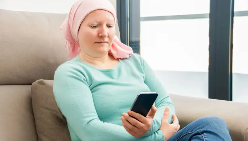 Kobieta w chustce na głowie, po chemioterapii, sprawdza telefon. Może szuka informacji o 500 plus dla chorych na raka ZUS.