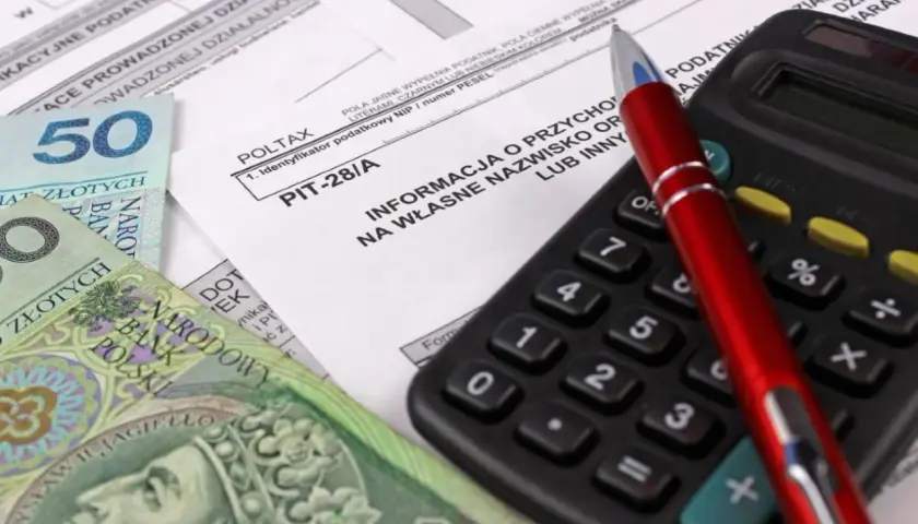 Formularz PIT-28/A, polskie banknoty, kalkulator i długopis.
