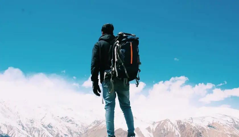 Un uomo con zaino in spalla ammira un panorama montano innevato. Il viaggiare da soli psicologia è un'esperienza di crescita.