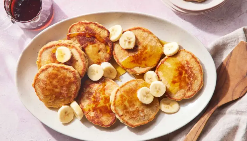 Tortitas de avena y plátano doradas, cubiertas con rodajas de plátano y sirope. Un desayuno delicioso y saludable.