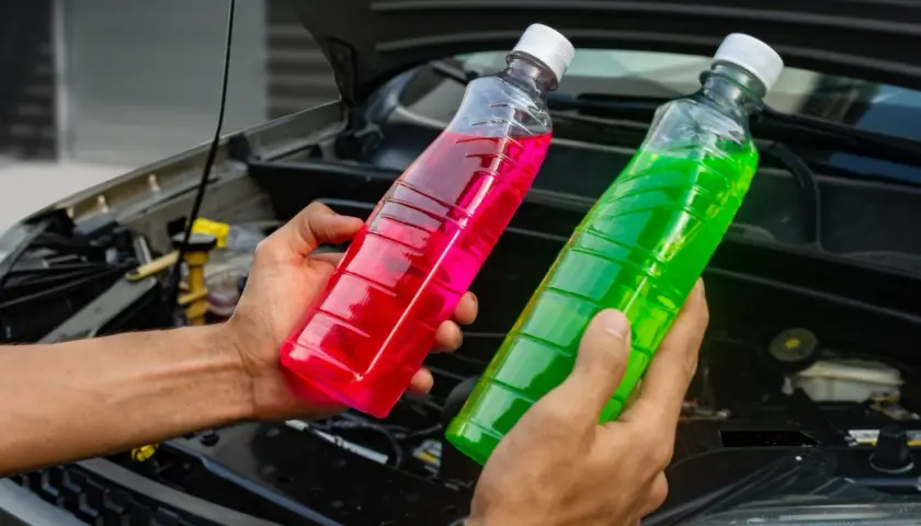 Manos sostienen botellas con líquido refrigerante de colores, rosa y verde, para el agua de motor coche.