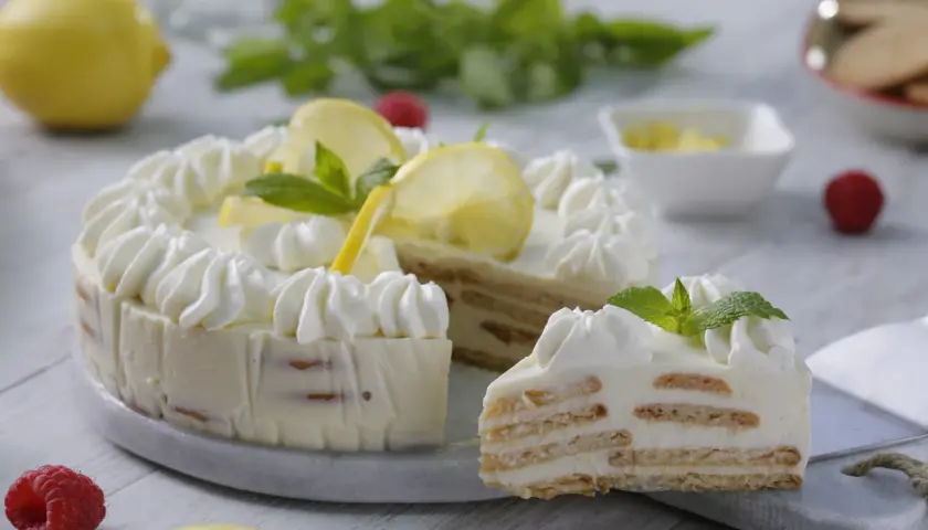 Delicioso postre de limón con leche condensada y galletas, decorado con crema batida, rodajas de limón y menta.