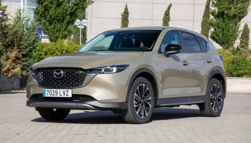 Un Mazda CX-5 2.2 150cv color bronce, con llantas negras y plateadas, estacionado en un día soleado. ¡Un coche ideal para tus viajes!