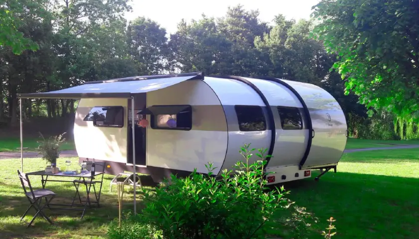 Une caravane XXL extensible, prête pour l'aventure, avec un auvent déployé et une table dressée sur l'herbe.