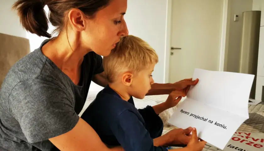 Mama uczy 5-latka czytać. Razem czytają tekst: "Rycerz przyjechał na koniu".