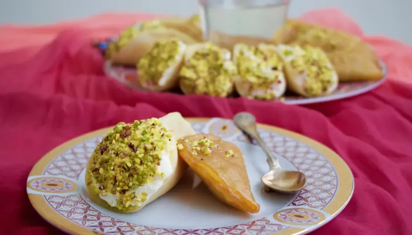 Atayef recept: söta pannkakor fyllda med grädde och pistagenötter, serverade på en tallrik med en sked.