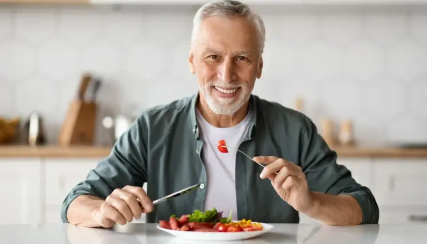 Uomo sorridente mangia cibo sano, godendosi ogni boccone con il suo impianto dentale.