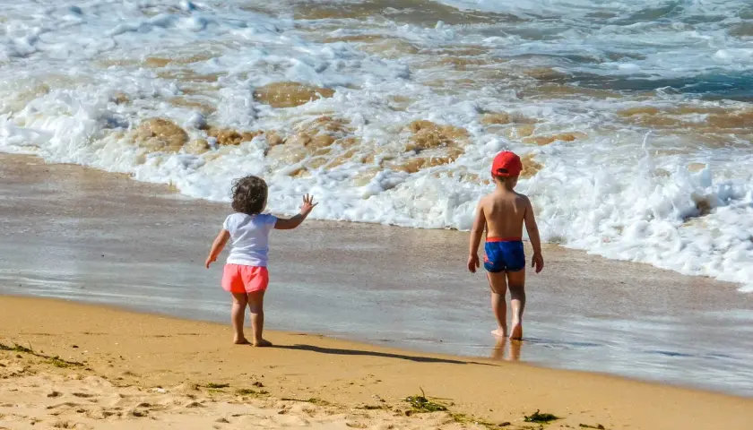 Dzieci w strojach kąpielowych dwuczęściowych dla dzieci bawią się na plaży, machając do fal.