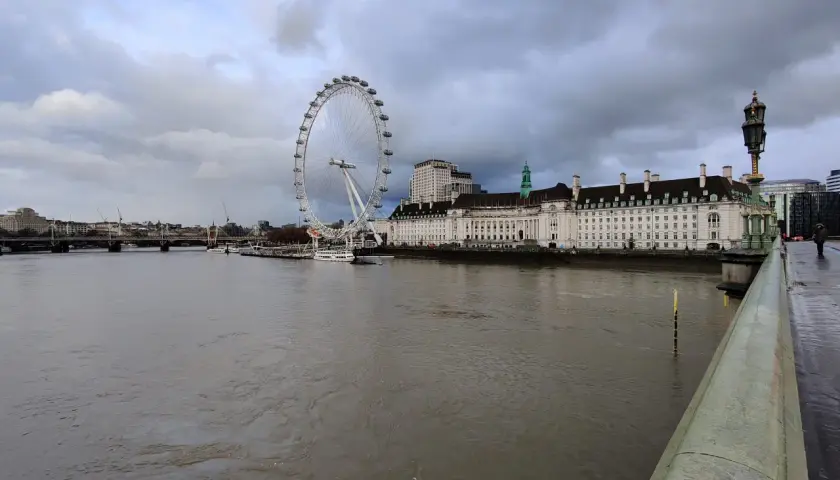 Widok na Tamizę z charakterystycznym London Eye w tle, pod pochmurnym niebem.