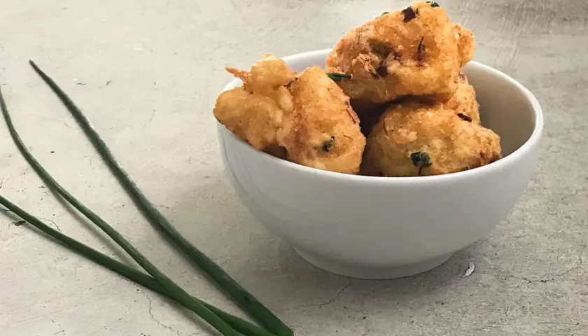 Tazón blanco con buñuelos de bacalao dorados y crujientes, decorado con cebollino fresco.