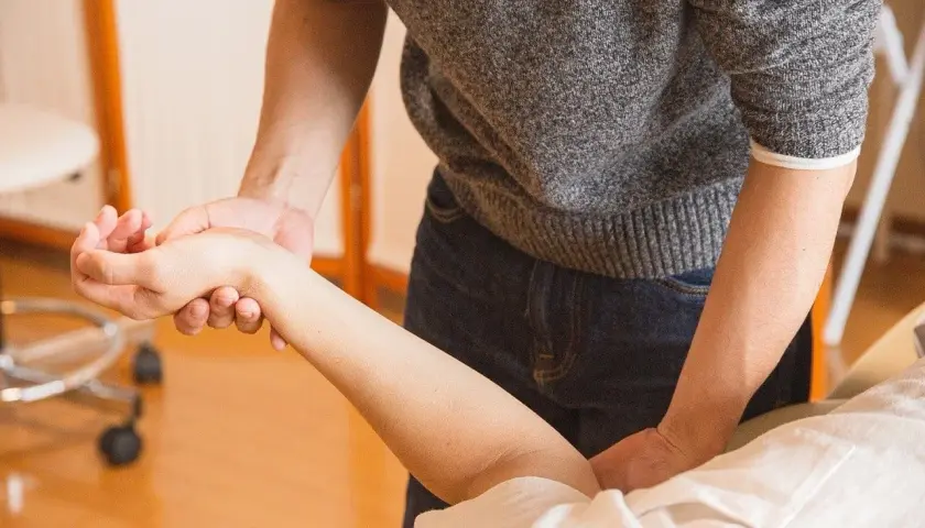 Fizjoterapeuta delikatnie masuje przedramię pacjenta, pokazując, jak leczyć łokieć tenisisty.