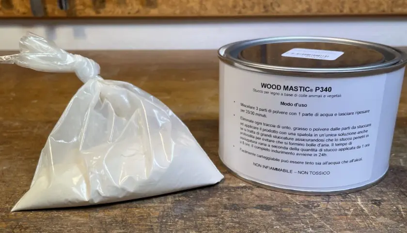 Sacchetto di stucco in polvere e barattolo di stucco per legno. Istruzioni su come si prepara lo stucco in polvere: mescolare 3 parti di polvere con 1 parte d'acqua.