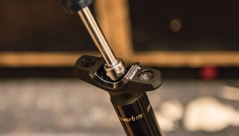 A socket wrench tightens a bolt on a Reverb Stealth dropper post.