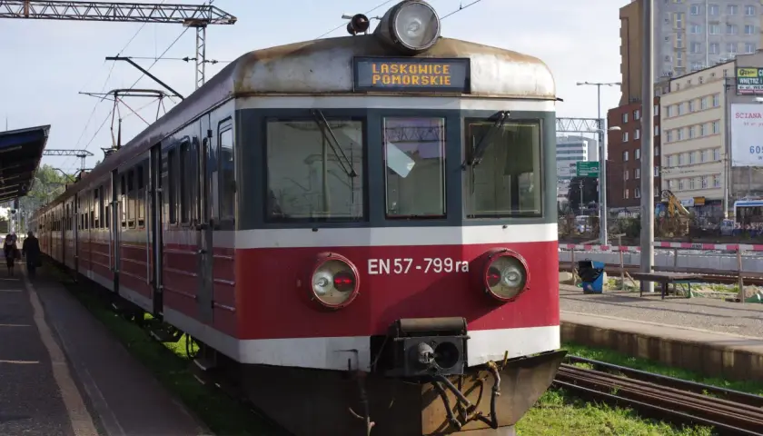 Pociąg EN57-799ra z napisem LASKOWICE POMORSKIE na tablicy. Stoi na peronie, w tle budynki i trakcje kolejowe.