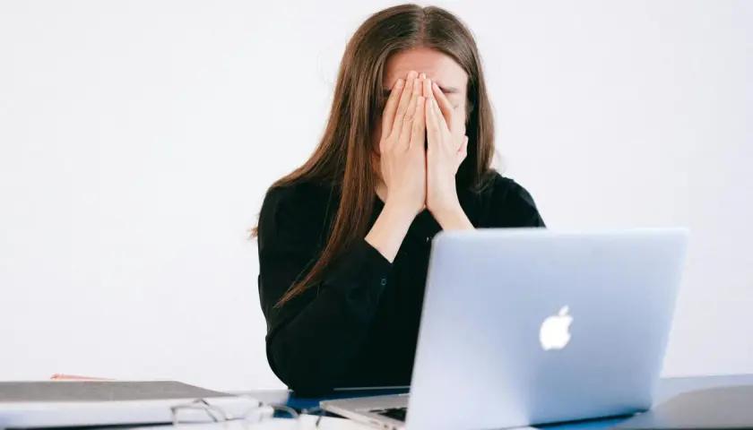 Mujer frustrada cubre su rostro, frente a un portátil. ¿Qué es un falso autónomo? Ejemplos de precariedad laboral.