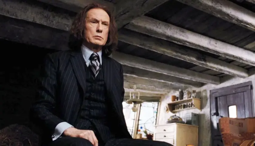Bill Nighy jako Rufus Scrimgeour w Harry Potterze, w garniturze, siedzi w ponurym wnętrzu.