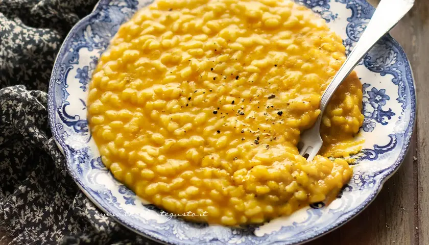 Un cremoso risotto zucca e rosmarino, servito su un piatto decorato, con una forchetta che affonda nella sua bontà.